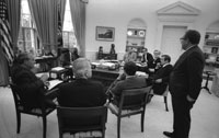 Secretary of State Henry Kissinger interrupts a meeting with senior advisers to relay the latest information on the U.S. evacuation of Saigon.  Oval Office.  April 29, 1975. 
