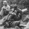 A grief stricken American infantryman whose buddy has been killed in action is comforted by another soldier. In the background a corpsman methodically fills out casualty tags, Haktong-ni area, Korea., 08/28/1950 