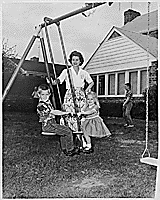 H0009-3. Betty Ford watches as Steve Ford and Susan Ford ride on a glider in the back yard of their home at 514 Crown View Drive, Alexandria, VA, as Michael Ford stands in the background. 1962.