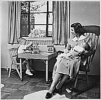 H0010-1. Betty Ford holds infant Jack Ford in her arms while Michael Ford plays at a small table in their apartment at 1521 Mount Eagle Place, Alexandria, VA. 1952.