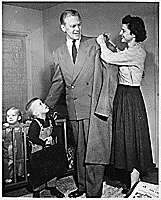 H0010-3. Betty Ford helps Gerald R. Ford, Jr., with his overcoat as Michael Ford and Jack Ford look on in their apartment at 1521 Mount Eagle Place, Alexandria, VA. 1953.
