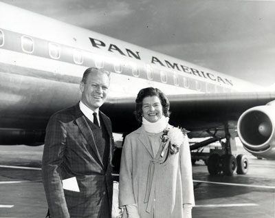 Representative Gerald R. Ford and wife Betty, wearing a neck brace for pain, stop for a photo in front of a Pan American jet at an unidentified airport. 