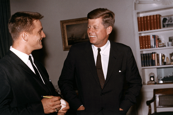 Home run champ Roger Maris, National Campaign Co-Chairman of the Multiple Sclerosis Society for 1962, signs a baseball for John F. Kennedy during a visit to the Oval Office.