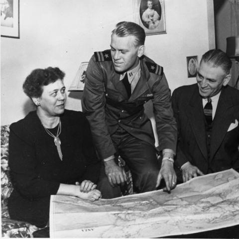 Gerald Ford, in his Naval uniform, sits with his parents, looking at a map