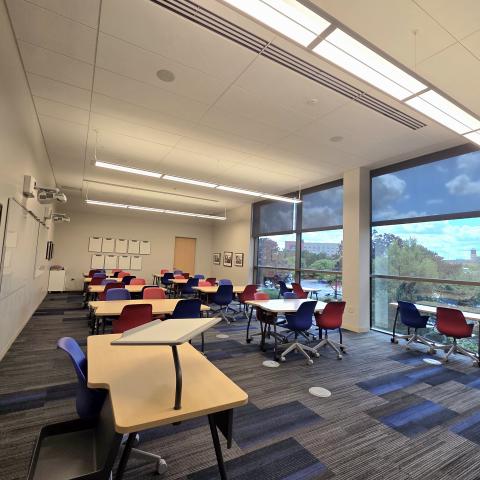 A small classroom with desks and colorful chairs is shown