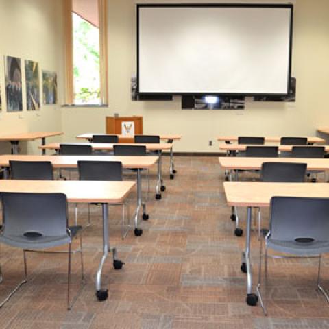 Rows of tables and chairs face a projector screen