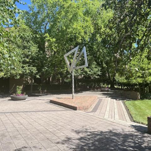 A brick patio with a green grass lawn is shown. A large, silver piece of art stands in the middle.