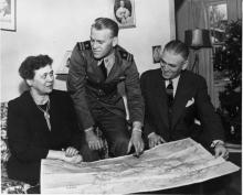 Gerald Ford, in his Naval uniform, sits with his parents, looking at a map