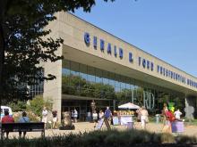 The plaza of the Ford Museum is shown with art displayed and people walking by.