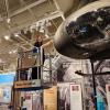 An intern standing on a lift, dusts a helicopter 