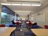 A classroom, with rows of desks and colorful chairs is shown