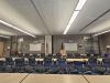 Rows of desks and chairs face a podium flanked by flags