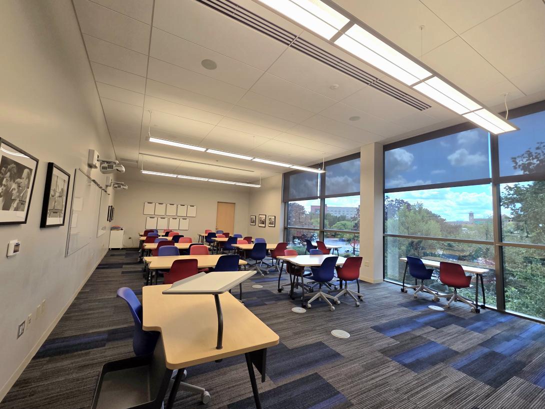 A small classroom with desks and colorful chairs is shown