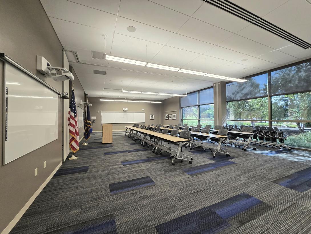 Rows of tables and chairs face a podium flanked by flags