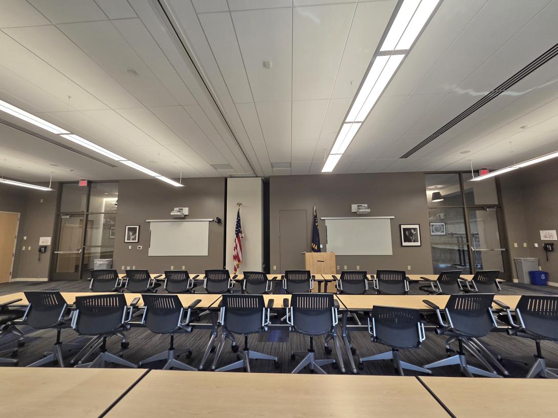 Rows of desks and chairs face a podium flanked by flags