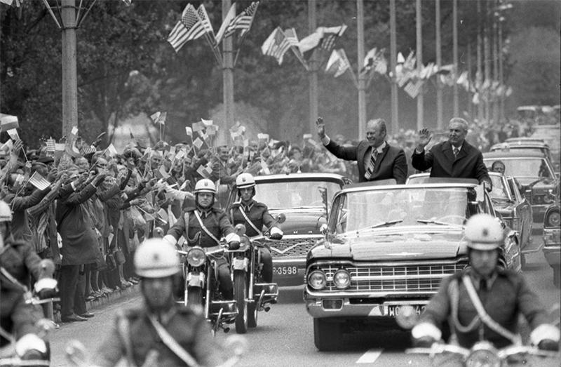 Gerald R. Ford waves to a crowd from a limousine during the motorcade From Okecie International Airport to Wilanow Palace
