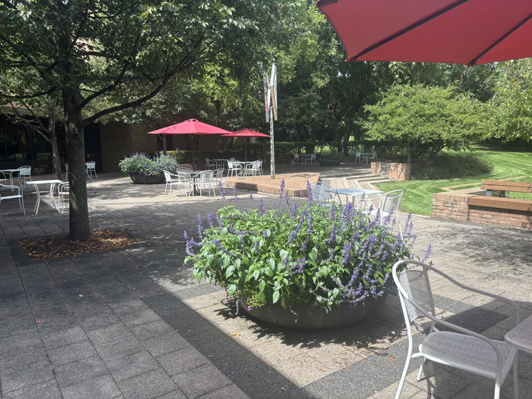 A brick patio, with tables, chairs, and red umbrellas is shown. 