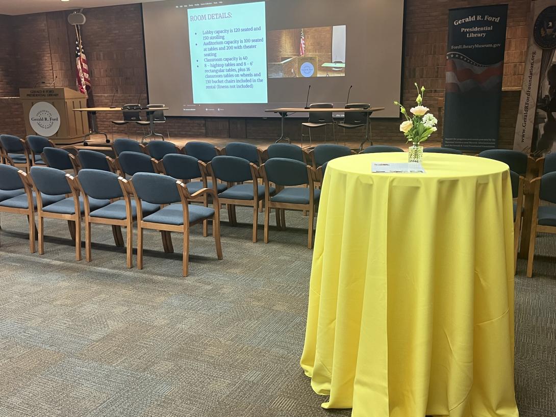 Rows of chairs face a stage with a projector screen. 