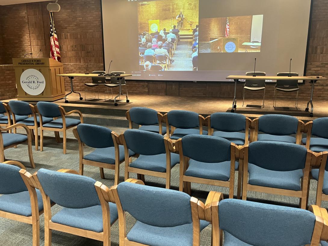 Auditorium stage has long tables and chairs set up for a panel discussion 