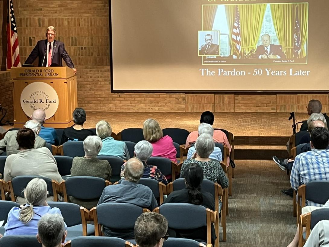 A speaker stands behind a podium on the stage in the auditorium 