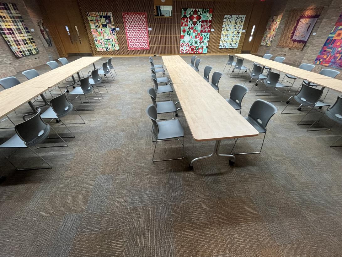 A large room is set up with long rectangular tables, surrounded by chairs. 