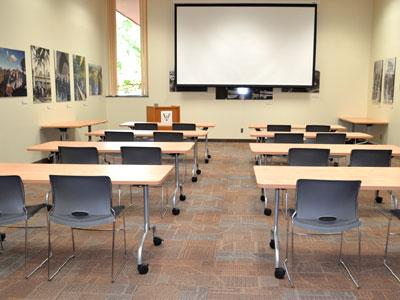 Rows of tables and chairs face a projector screen